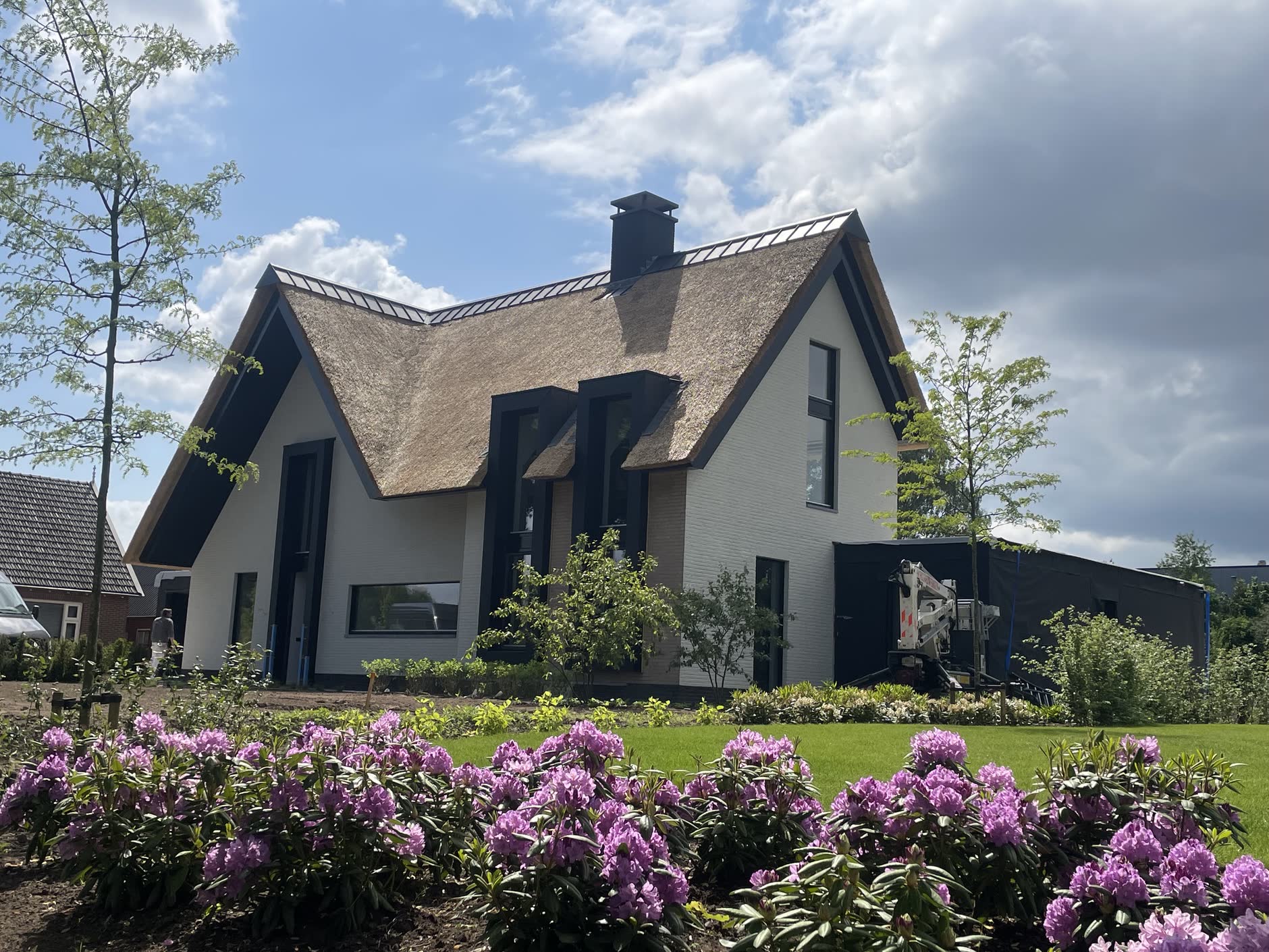 Villa met rieten kap, witte gevel en donkere kozijnen achter bloeiende rododendrons